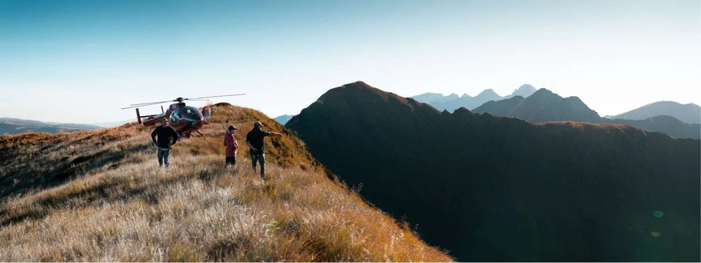 Hunters walking along a golden ridge beside a landed helicopter