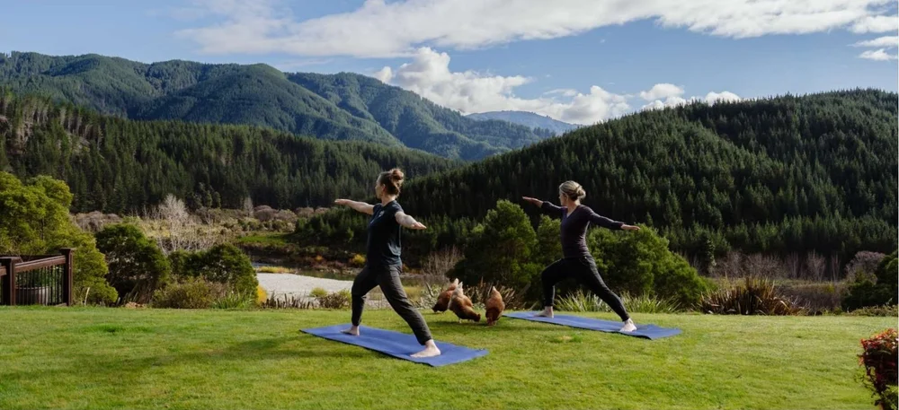 Two guests practising yoga on the lawn at Stonefly Lodge with forested hills behind