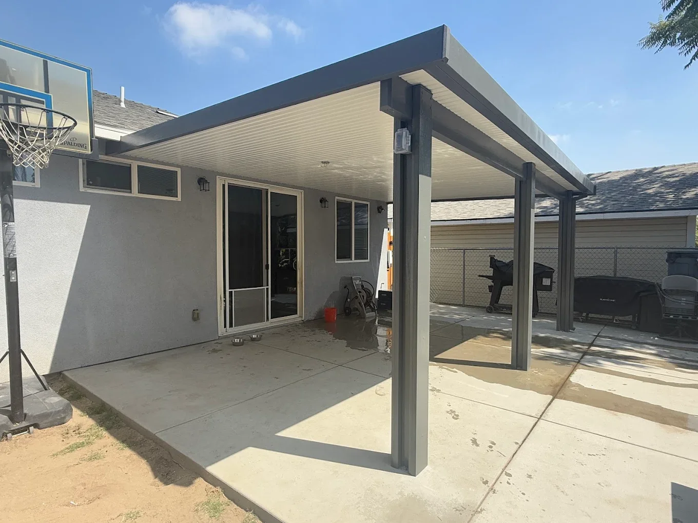 Backyard patio with a covered area, a sliding glass door, and outdoor furniture, including a barbecue grill and chairs.
