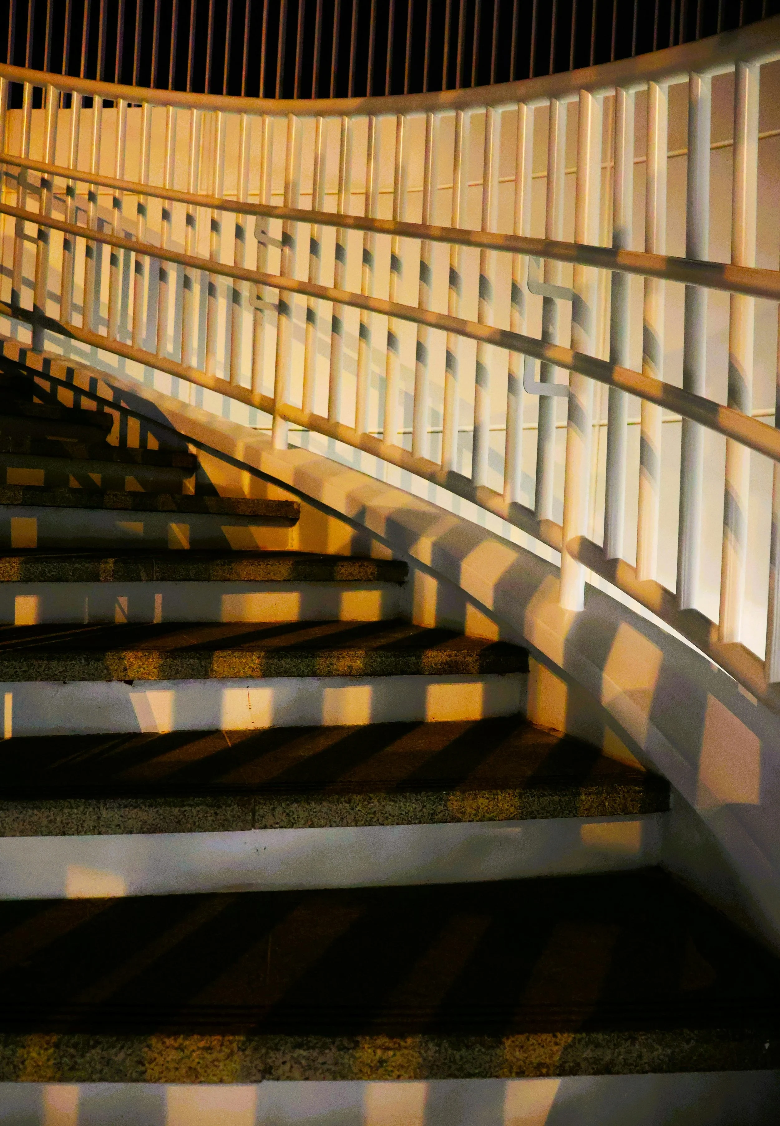 Night view of outdoor stairs with gray steps and white railings cast long shadows from nearby lighting.
