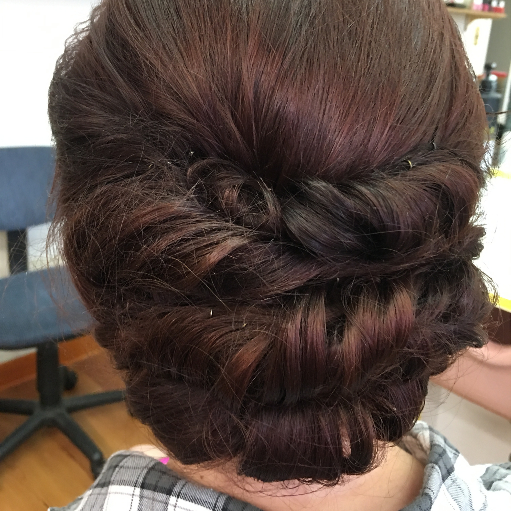 Back of a woman's head with a styled updo featuring braids and curls, with reddish-brown hair color.