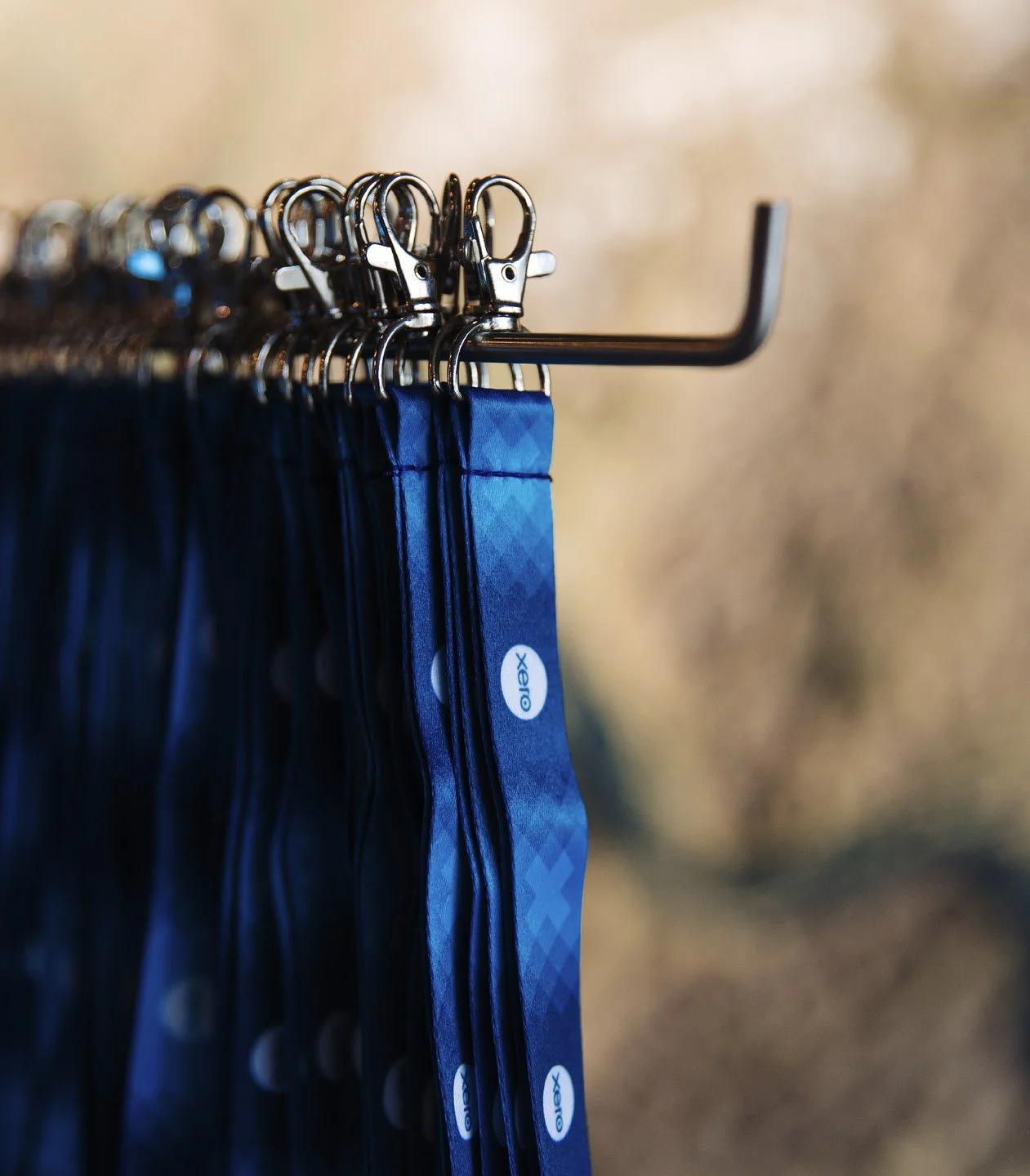 Blue fabric lanyards hanging on a metal rod with hooks against a blurred background.