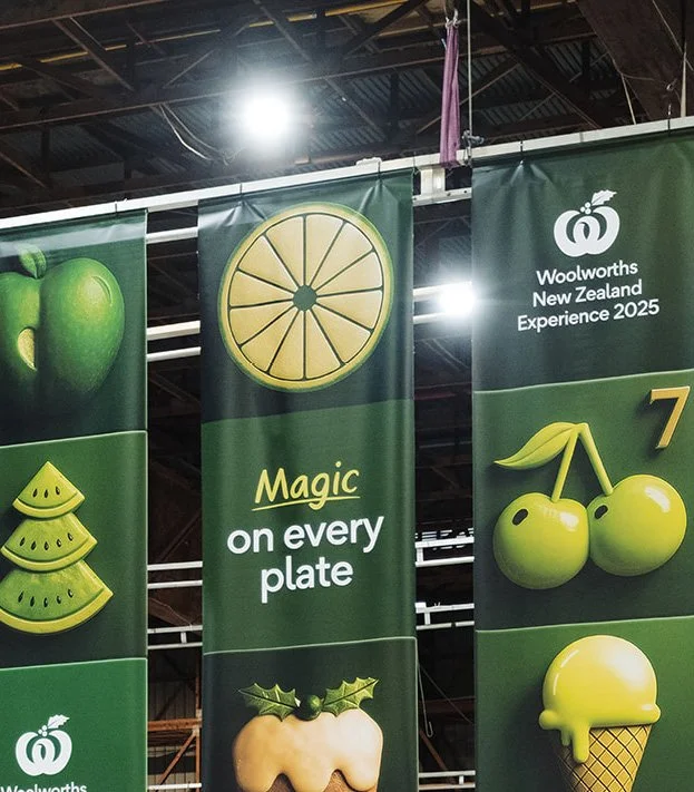 Display banners at Woolworths New Zealand during the 2025 Experience, showcasing various green fruits and desserts.