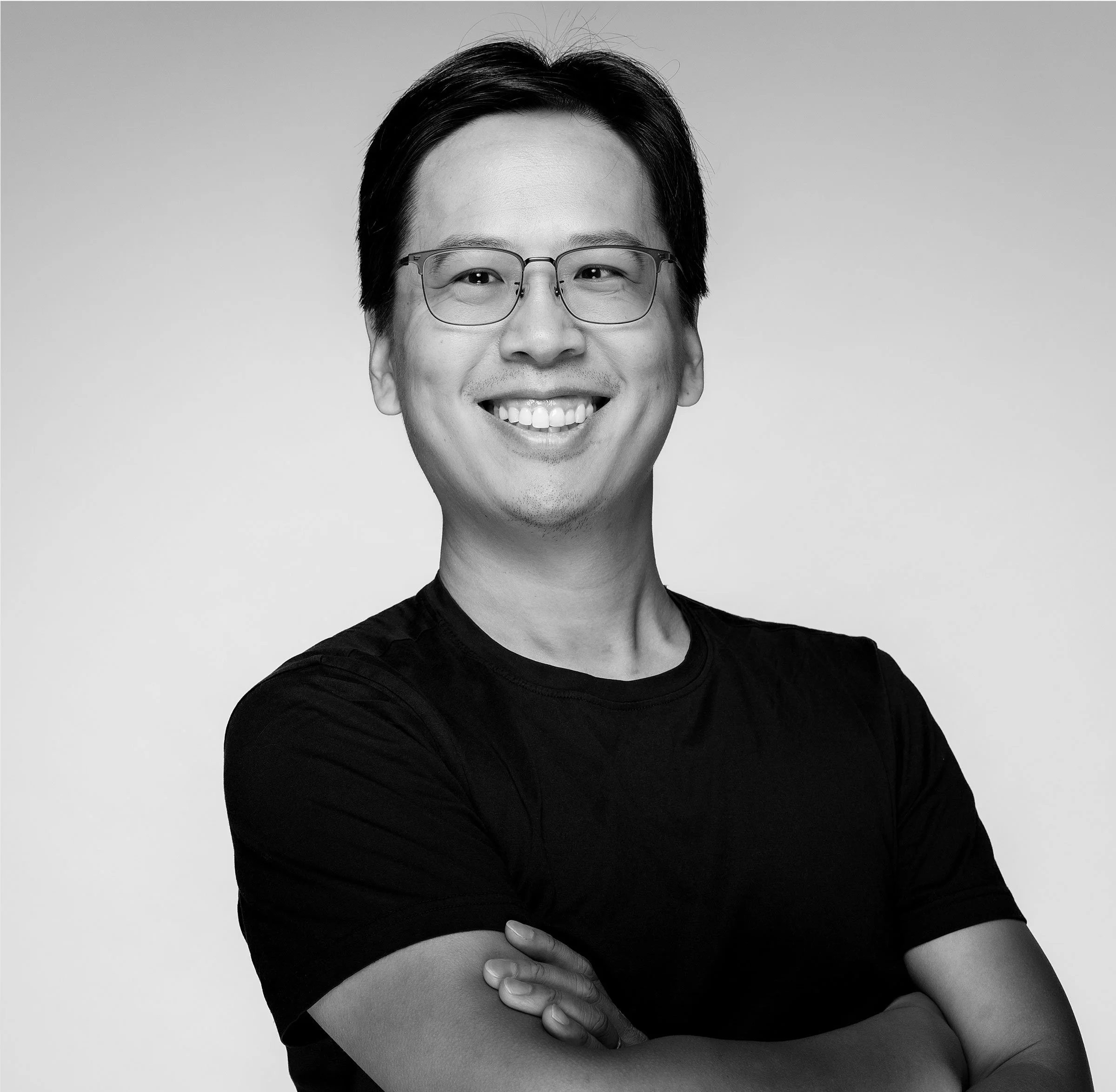 Black-and-white photo of a smiling man with glasses wearing a collared shirt and a sweater with a V-neck.