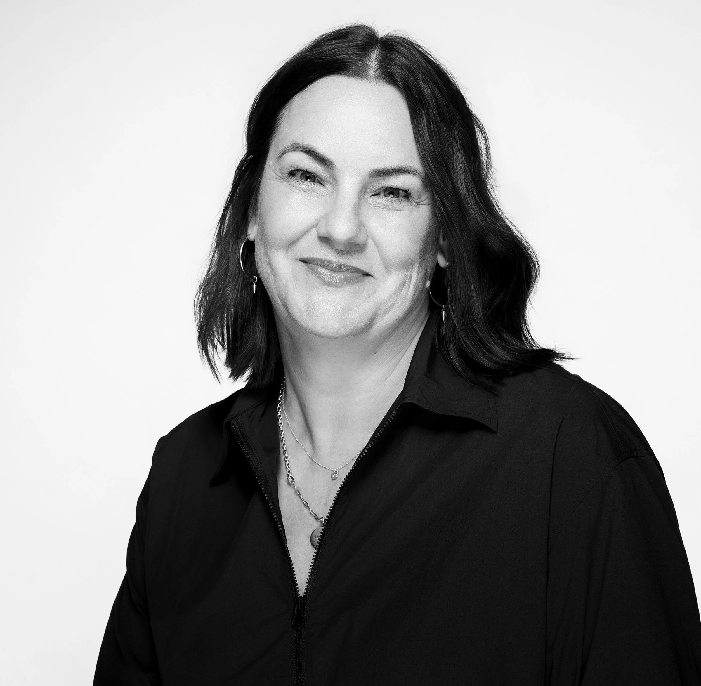 Black and white portrait of a smiling woman with shoulder-length hair wearing large star-shaped earrings and a T-shirt with a heart design.