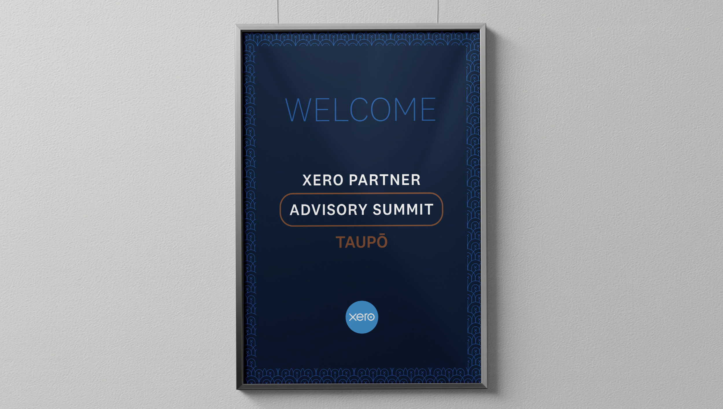 Framed poster on a wall welcoming attendees to the Xero Partner Advisory Summit in Taupō, featuring a blue background with decorative borders, the Xero logo at the bottom, and event details in white and brown text.
