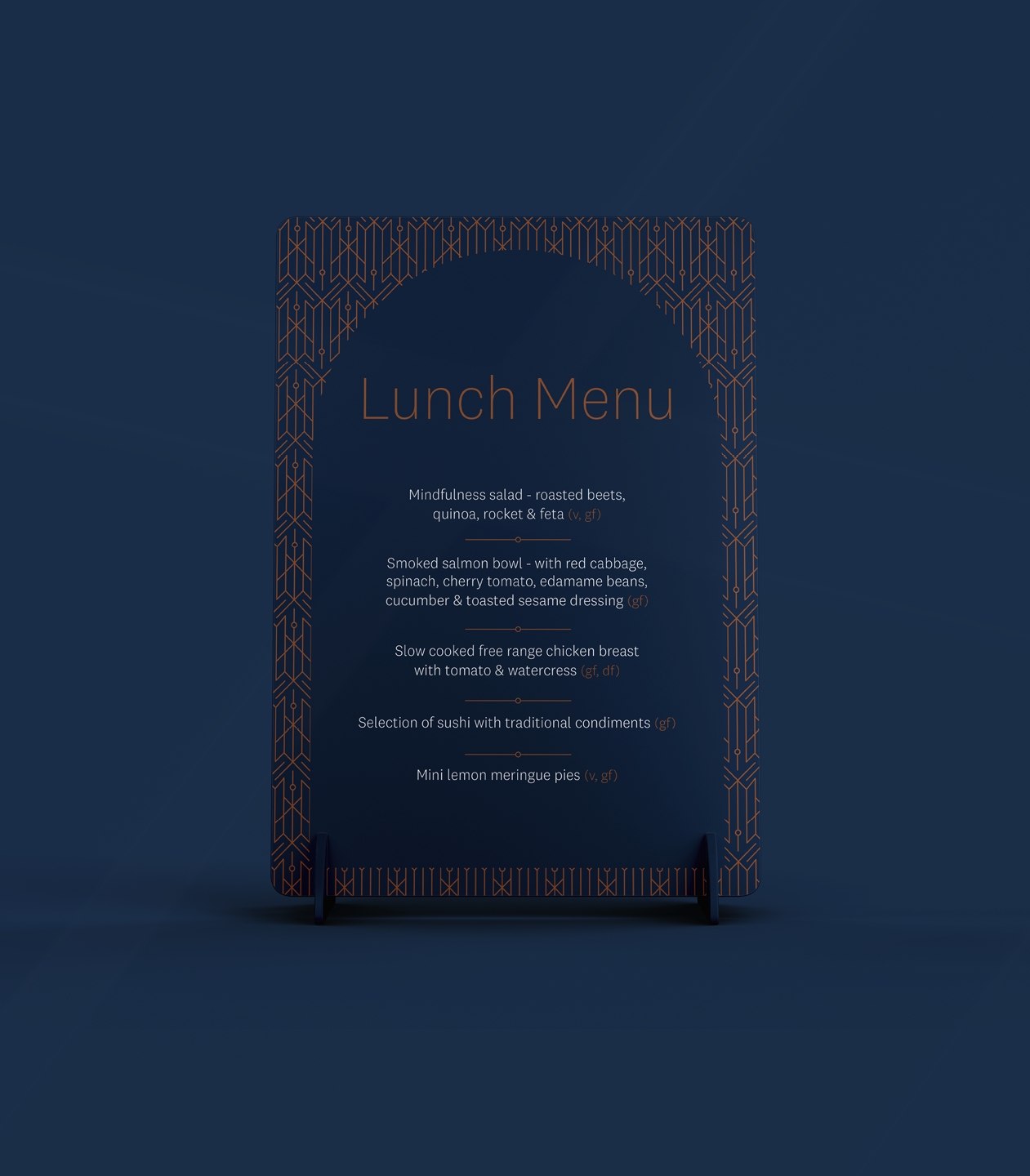 Dark blue lunch menu sign with geometric gold border design, listing various meal options including salads, salmon bowl, chicken breast, sushi, and lemon meringue pies.