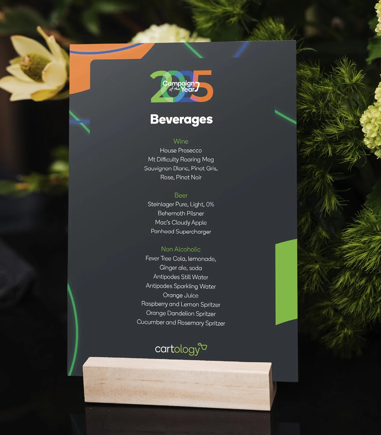 Menu board listing beverages such as wine, beer, and non-alcoholic drinks at an event, with a colorful design and the logo 'cartology' at the bottom.