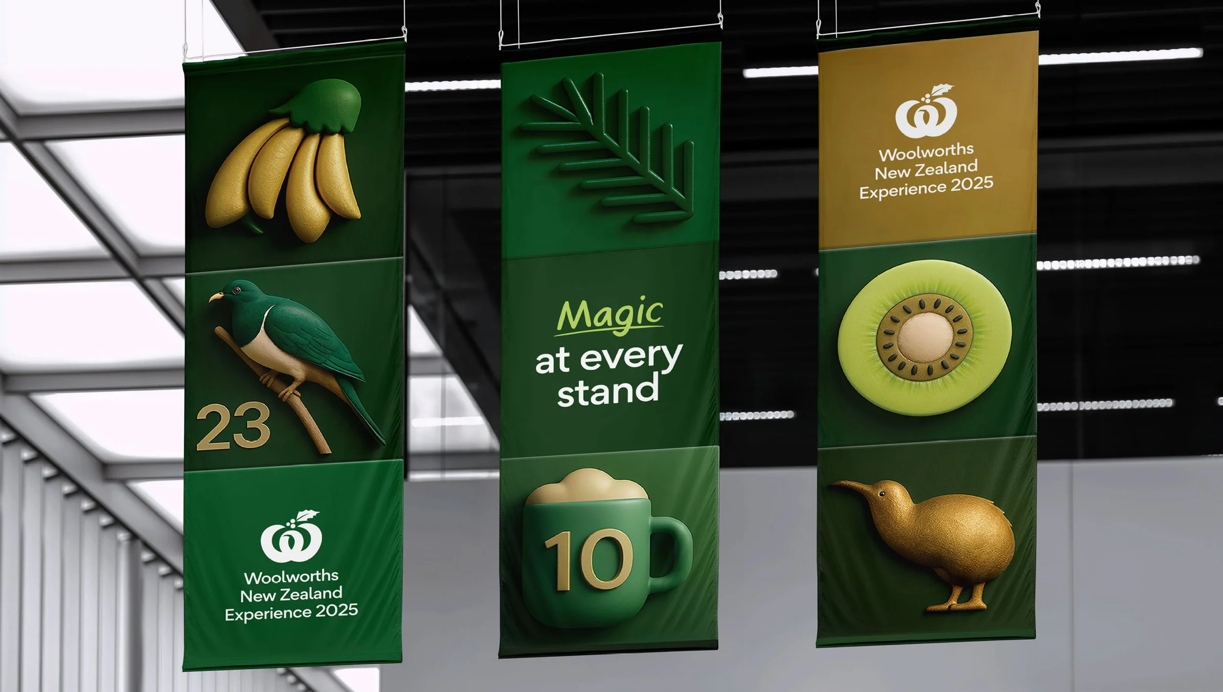 Three vertical banners hanging indoors at Woolworths New Zealand Experience 2025. The banners are green with gold and white accents, displaying images of bananas, a bird, a mug with the number 10, a kiwi, a kiwi fruit slice, and text reading 'Magic at every stand' and 'Woolworths New Zealand Experience 2025.'