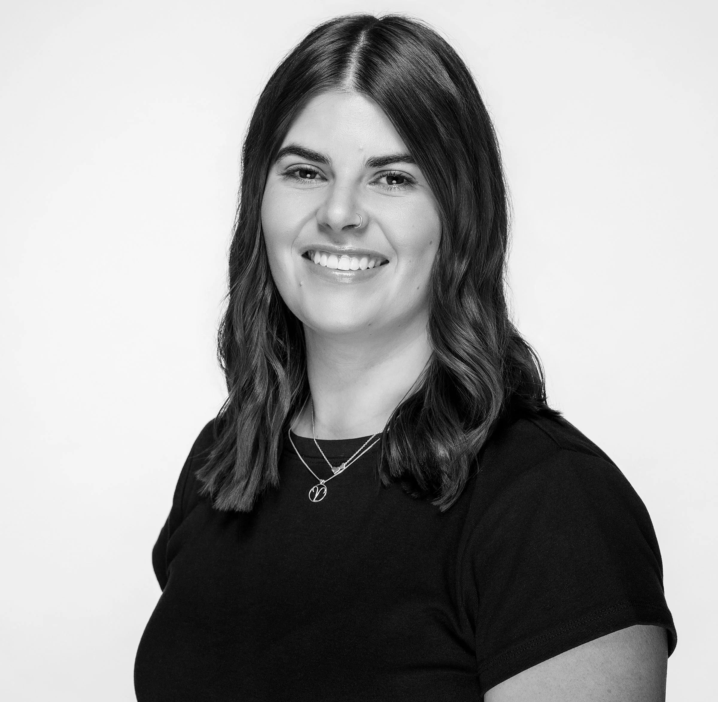 Black and white photo of a woman smiling, wearing a black t-shirt and layered necklaces.