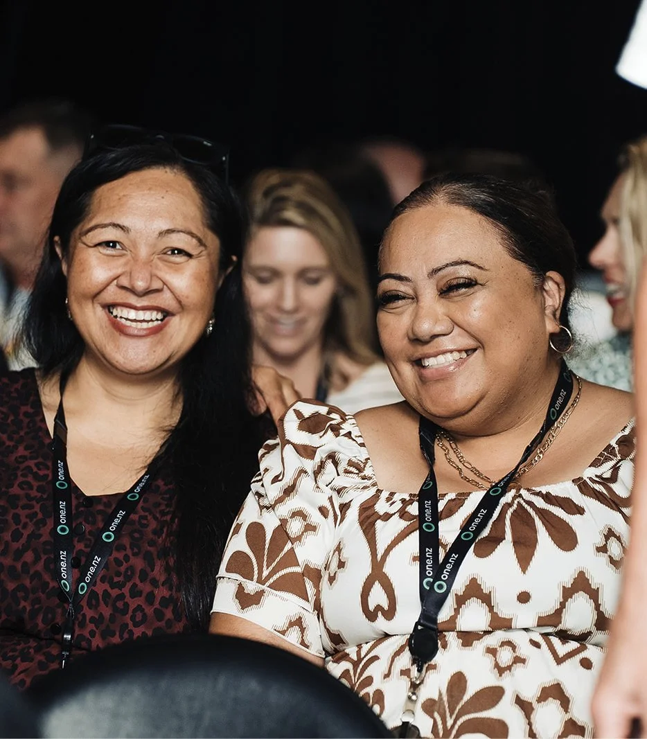 Two women smiling and talking at a conference or event, wearing lanyards.