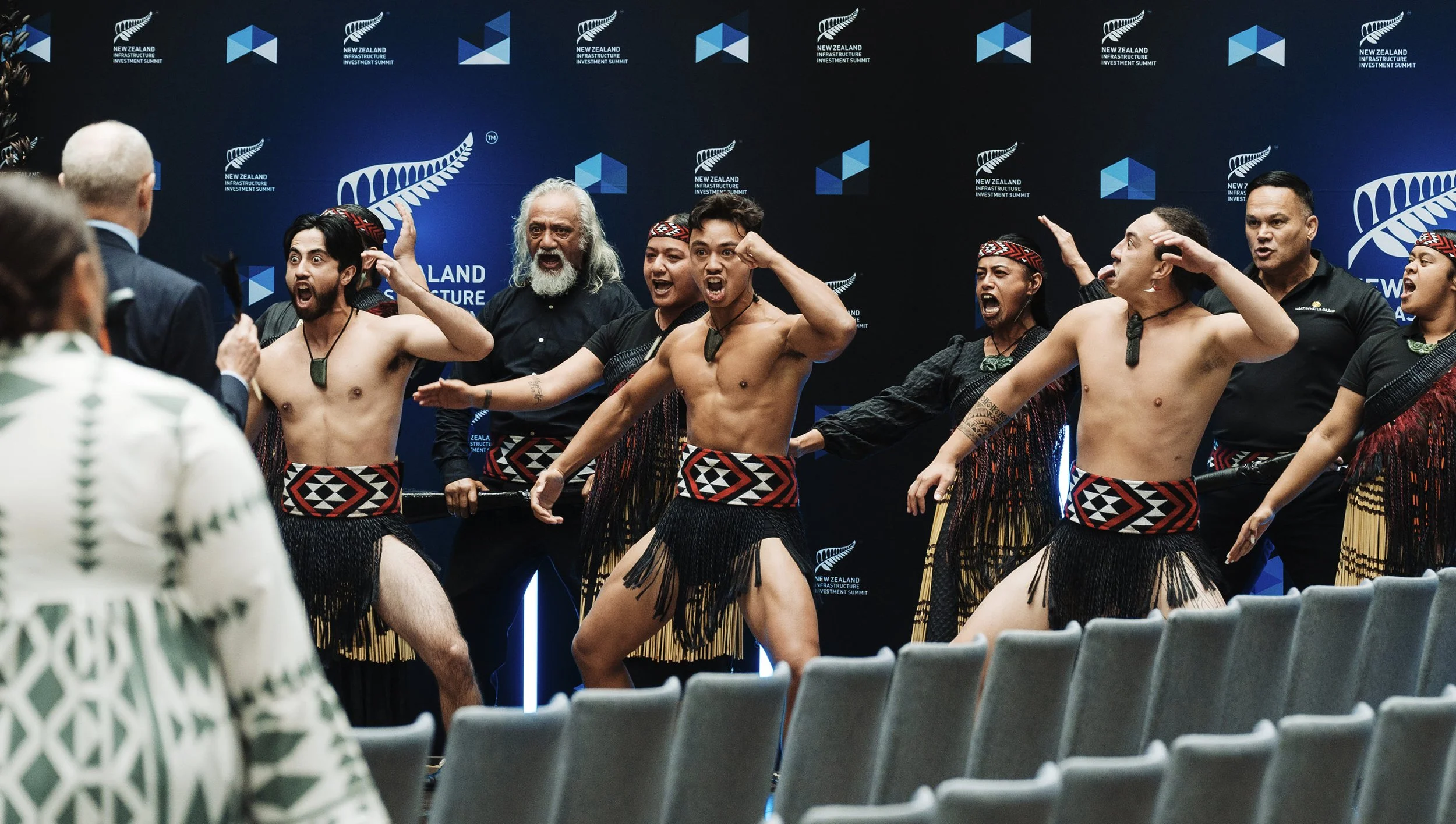 Indigenous performers performing haka dance at the New Zealand Infrastructure Investment Summit, with a panel of speakers in the foreground.