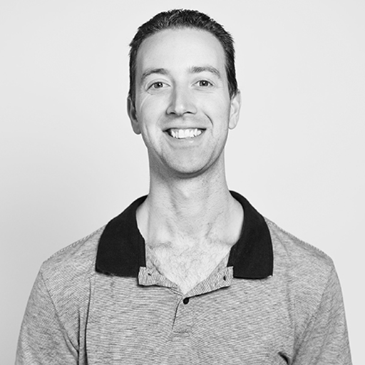 A black-and-white portrait of a man smiling, wearing a collared shirt, against a plain background.