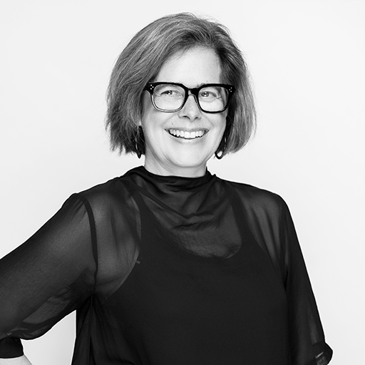 Black and white photo of a smiling woman with short hair and glasses, wearing a black sheer blouse.