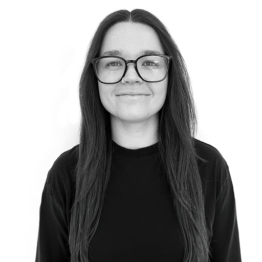 A young woman with long dark hair, wearing glasses and a black top, smiling at the camera against a plain white background.