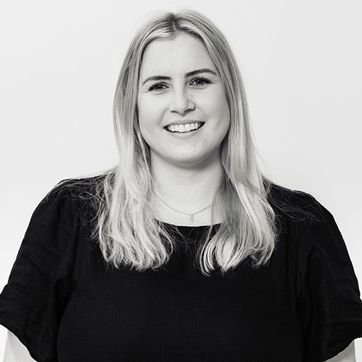 Black and white photo of a smiling young woman with shoulder-length blonde hair, wearing a dark top, against a plain white background.