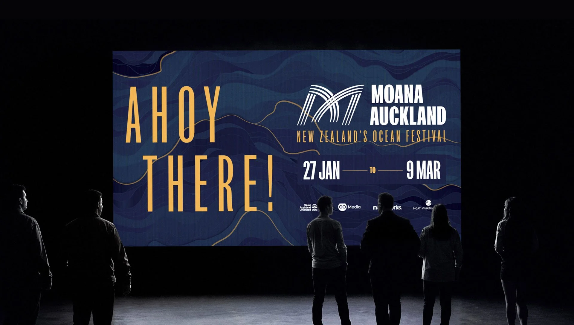People watching a large digital screen with event information about Moana Auckland Ocean Festival, held from January 27 to March 9, 2023.