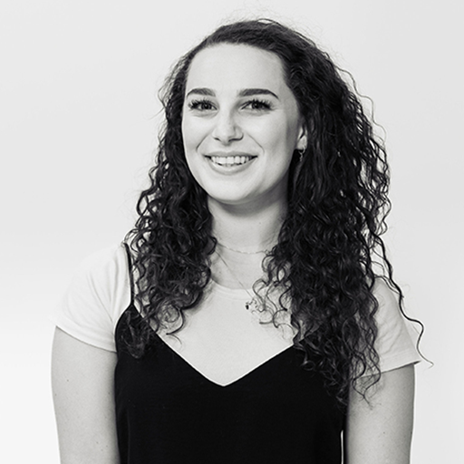 Black and white portrait of a smiling woman with curly hair, wearing a light-colored t-shirt and a dark sleeveless top.