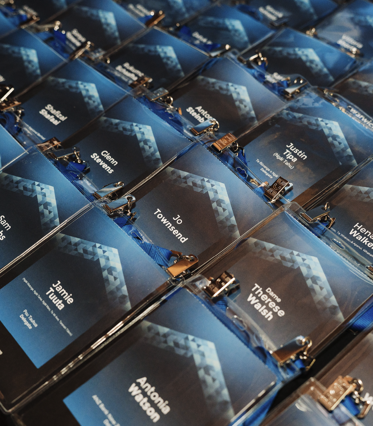 Name tags with blue backgrounds and geometric designs, attached to clear plastic holders with metal clips.