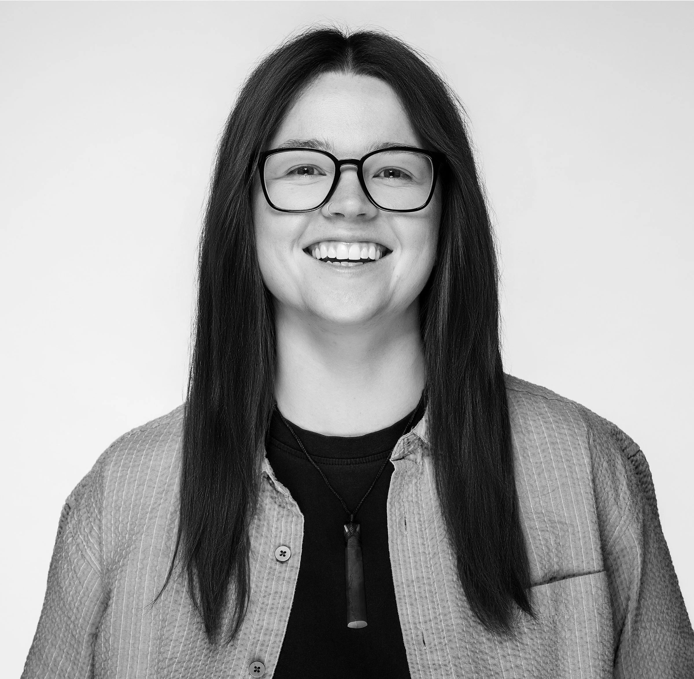 A young woman with long dark hair, wearing glasses and a black top, smiling at the camera against a plain white background.