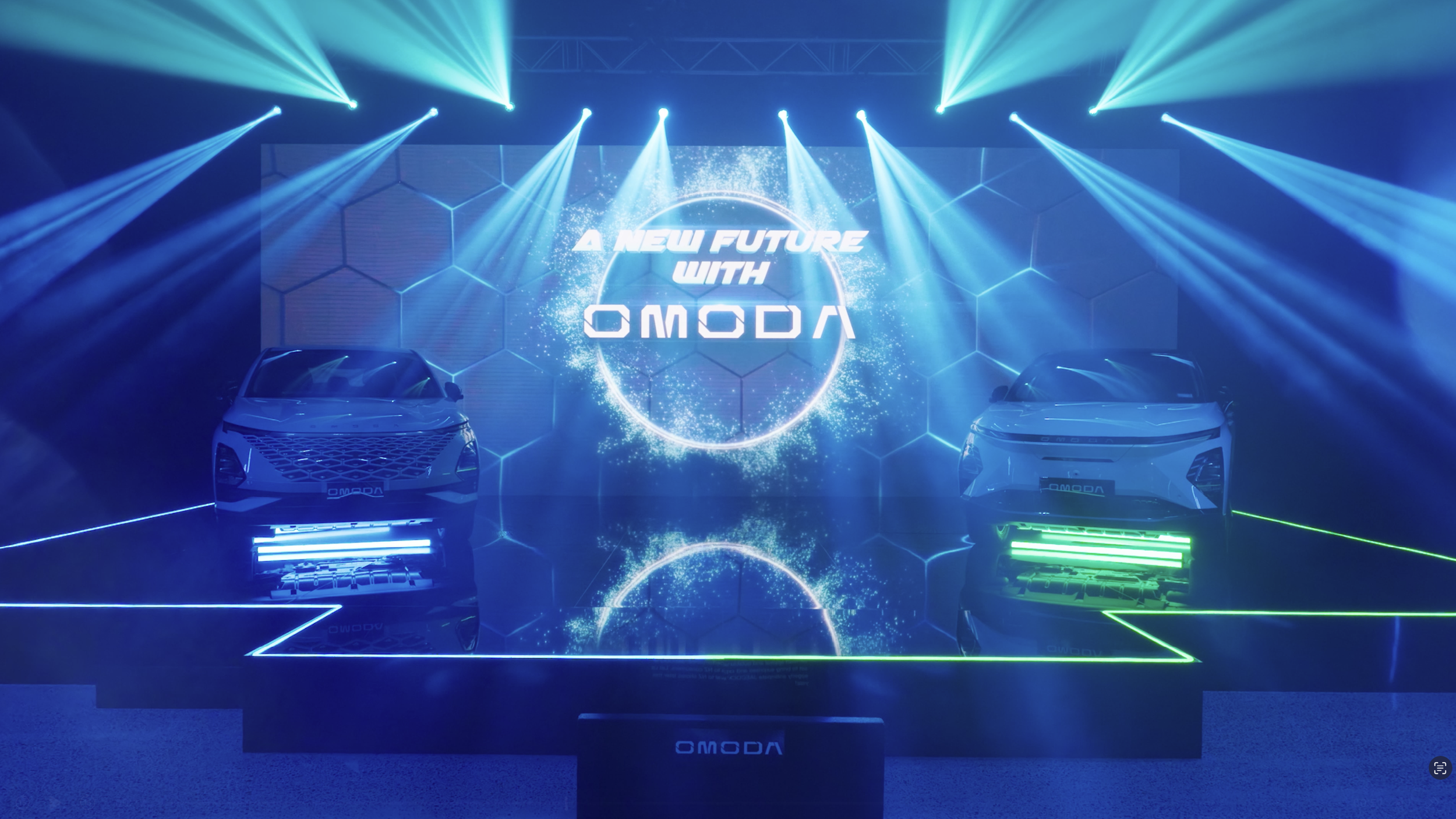 Two futuristic cars on display at an event with bright blue and green lighting, a large screen in the background showing the words 'A New Future with Omoda' and a digital illustration of a globe.