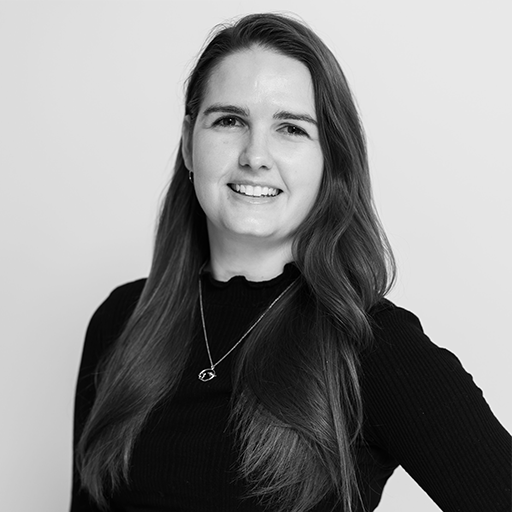 Black and white photo of a woman with long hair, smiling, wearing a black top and a necklace, against a plain background.