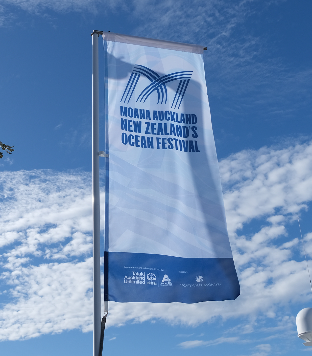 Flag for Moana Auckland New Zealand's Ocean Festival flying in the wind against a blue sky with clouds.