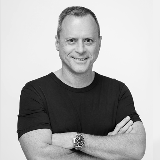 Black and white portrait of a man with short hair, smiling, wearing a black T-shirt and a smartwatch, with arms crossed.
