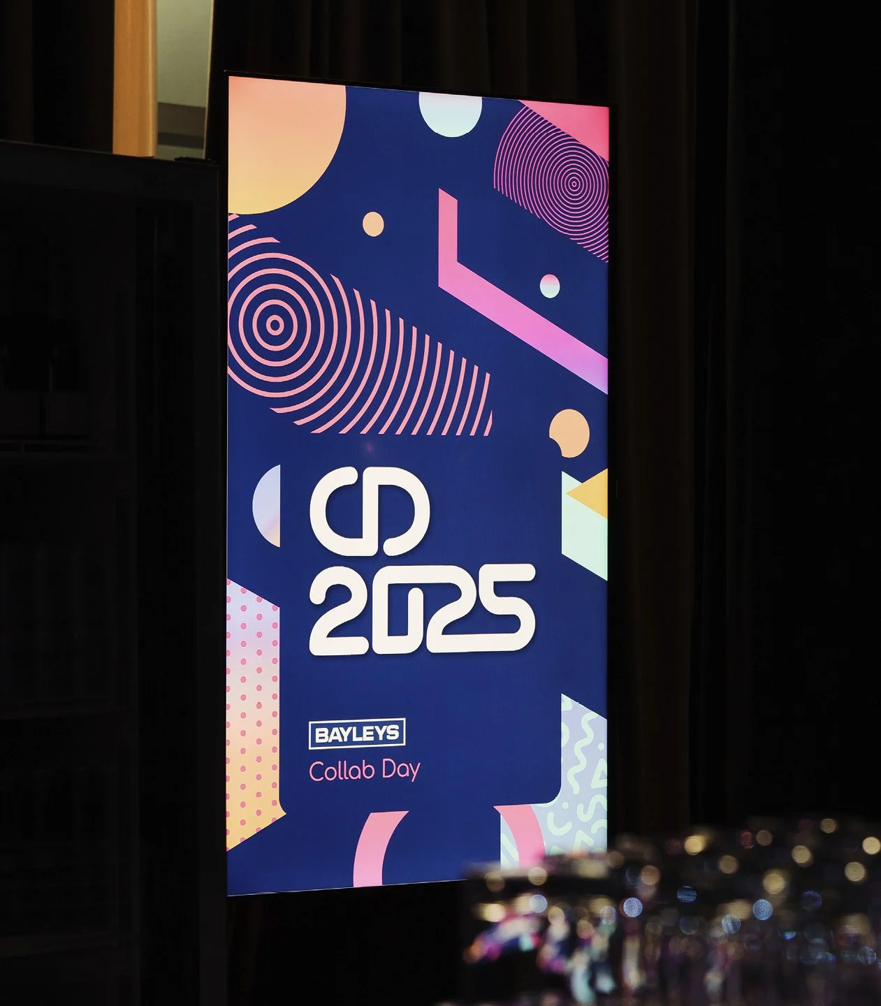 Digital display reading 'CD 2025' with 'Bayleys Collab Day' below, featuring colorful, abstract geometric patterns on a dark background.