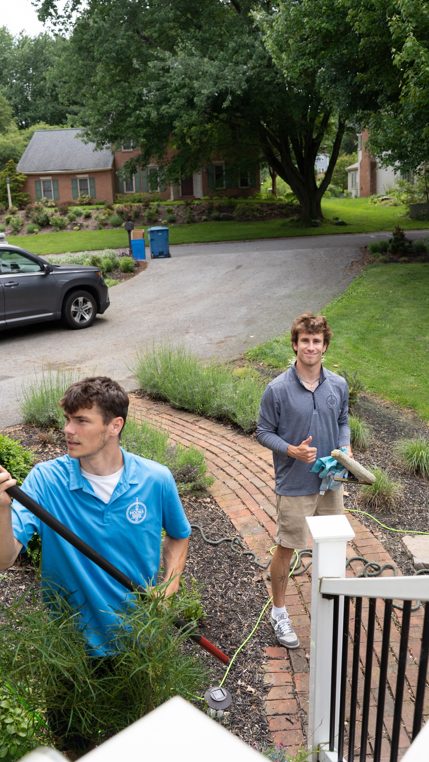 Two Hooks Property Services crew members cleaning windows at a home, one giving a thumbs up