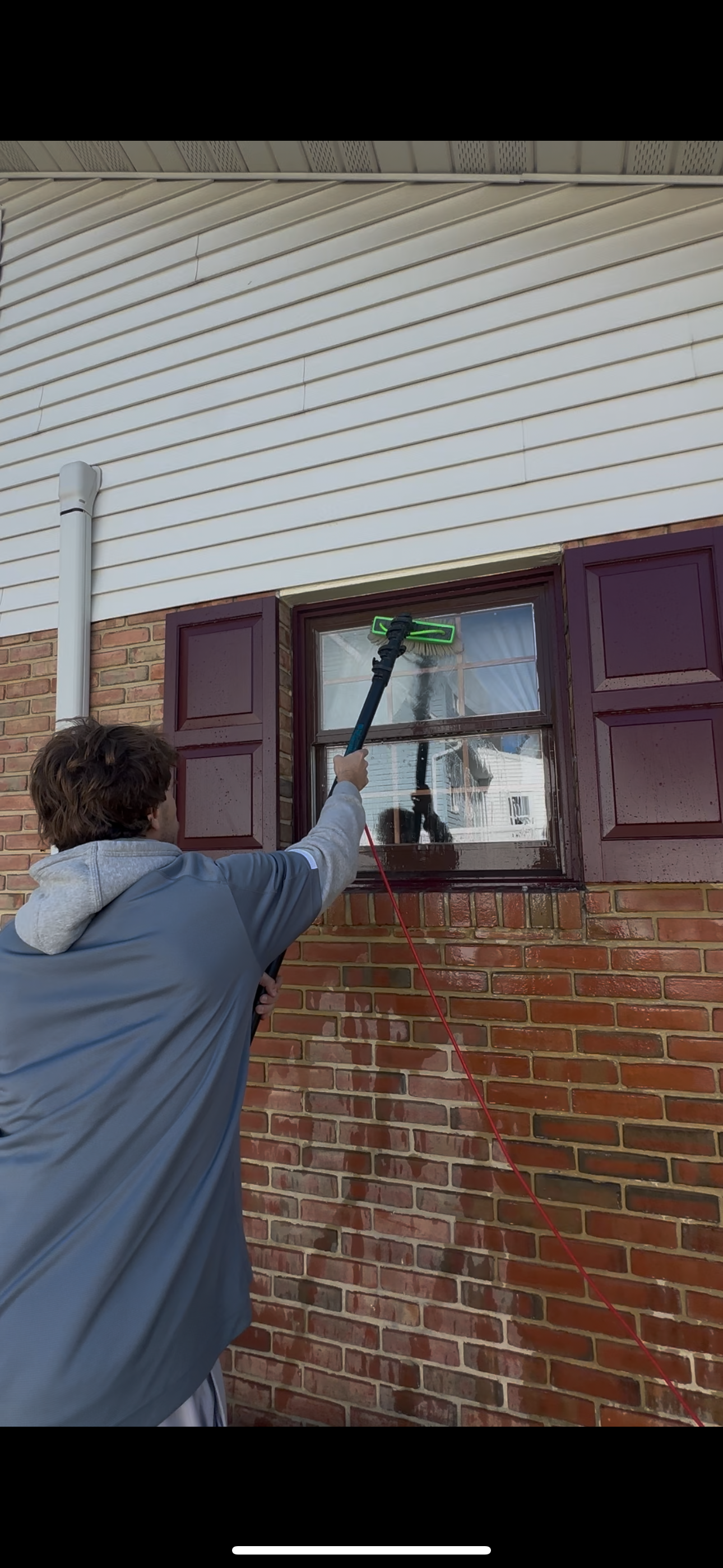 A man cleaning a window from outside, wearing yellow rubber gloves and a uniform, with cleaning supplies on the window sill.
