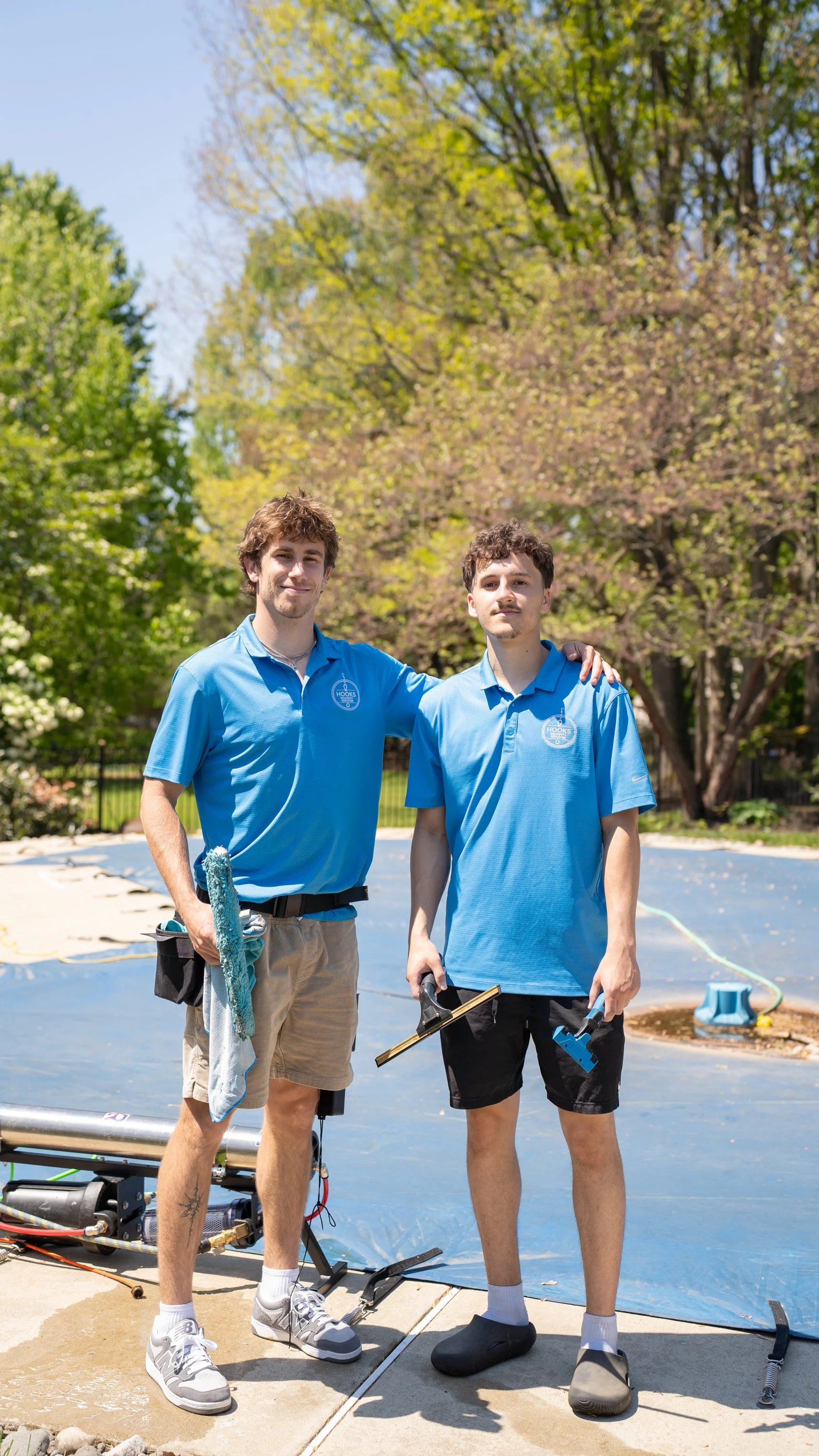Two Hooks Property Services team members in blue polos holding window cleaning tools