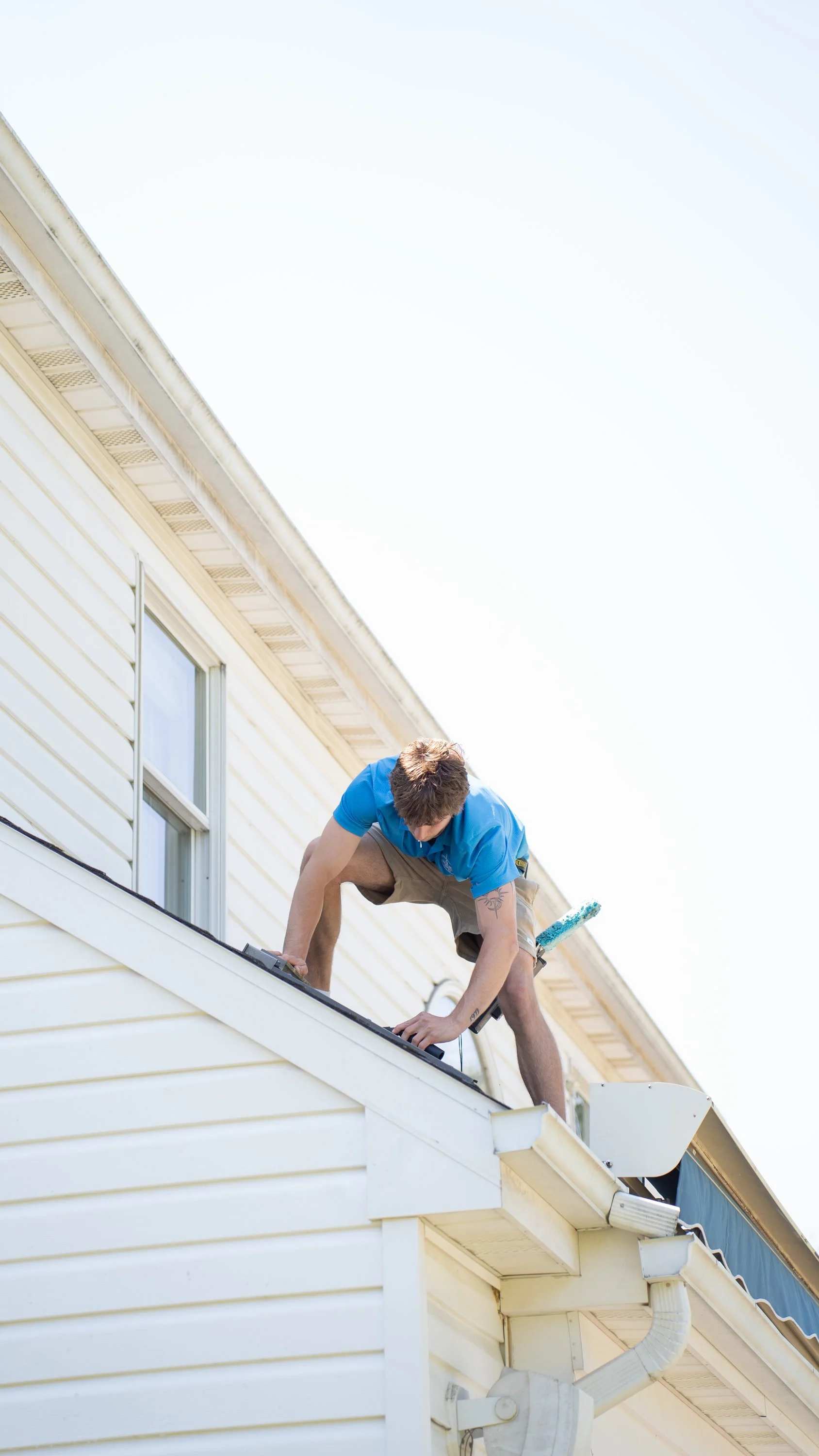 Hooks Property Services technician working on a roof beside an upstairs window