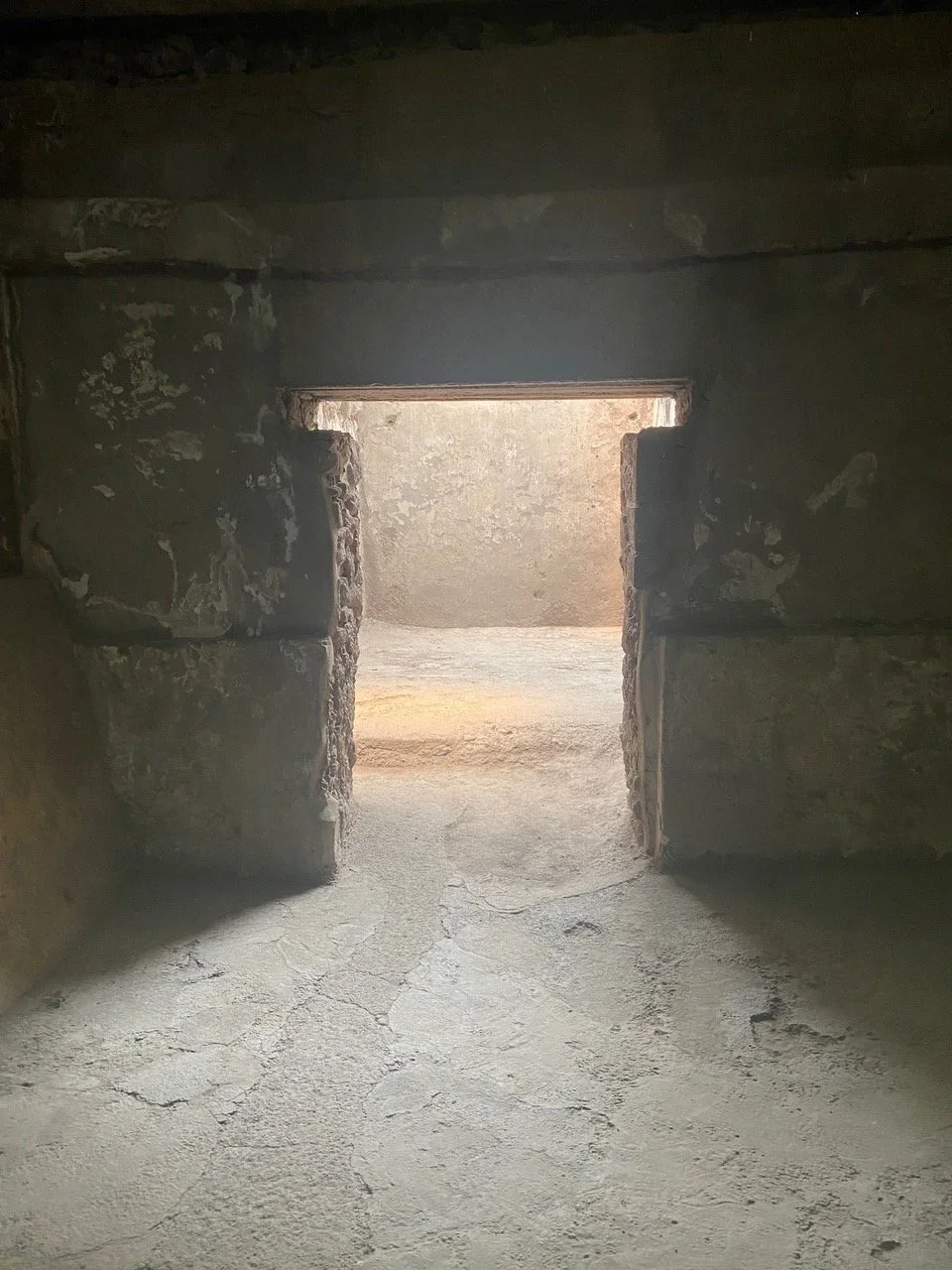 View of a stone doorway with sunlight outside, cracked concrete floor inside