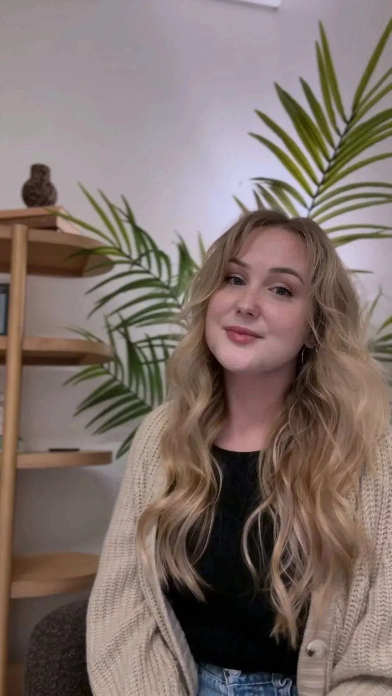 Kayla Hawking, Associate Marriage and Family Therapist in California, seated in a therapy office with wooden shelves and plants behind her.