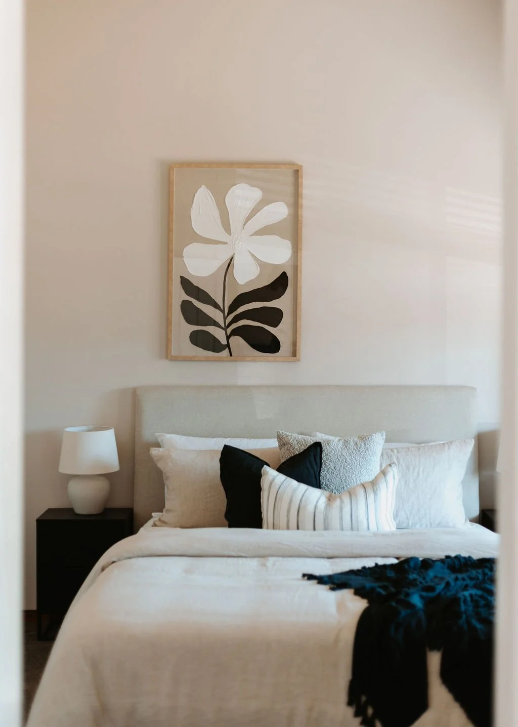 A circle shaped image of a styled master bedroom in coastal neutrals with a flower painitng feature on the wall at a Gosford home.