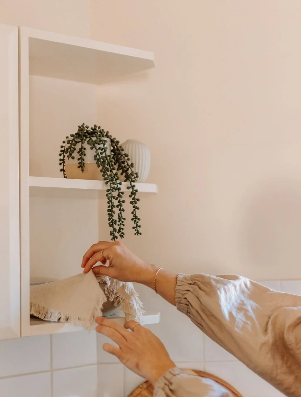 A hand reaching to style a potted plant on a shelf in the kitchen.