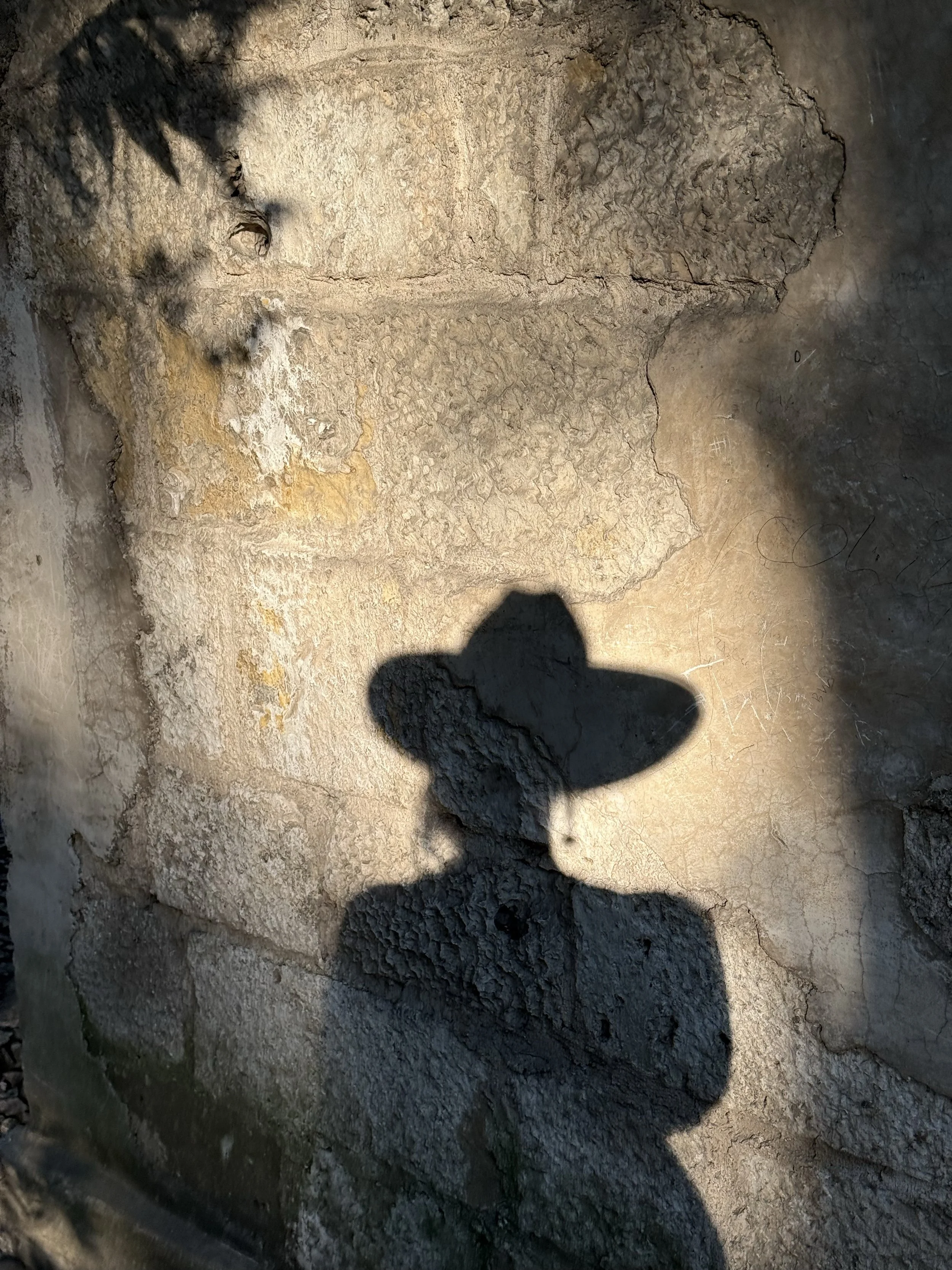 The shadow of a person wearing a wide-brimmed hat is cast on a textured stone wall.