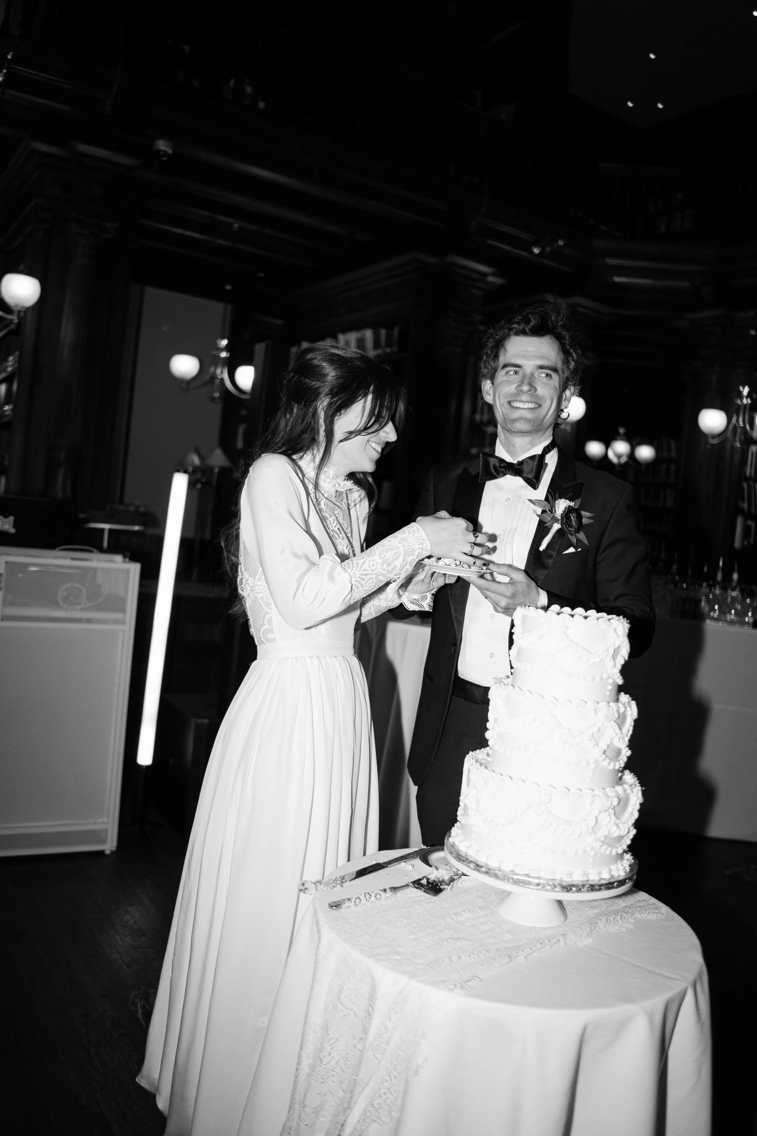 A bride and groom cutting a wedding cake together in an elegant, wood-paneled room.