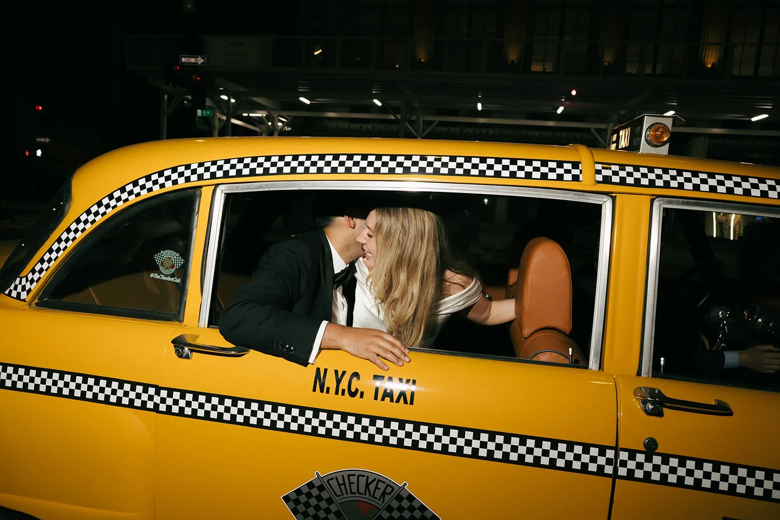 A couple is sharing a kiss inside a yellow NYC taxi at night.