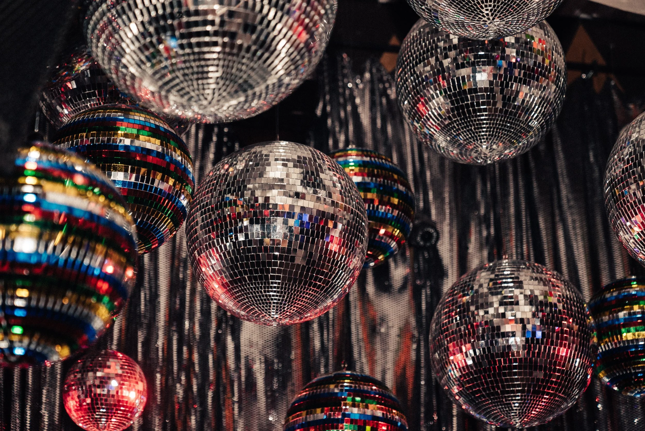 Multiple disco balls hanging against a dark, fringed backdrop.