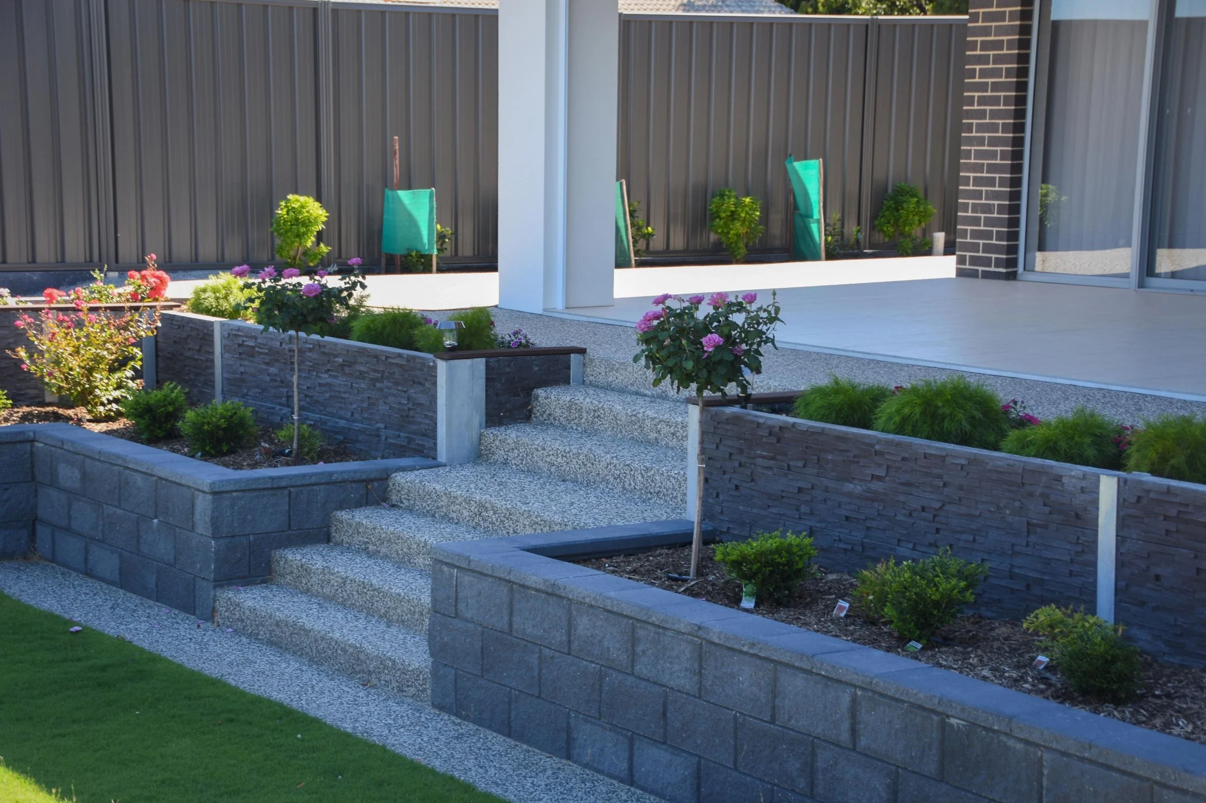 Two level concrete sleeper and stone retaining wall structure featuring garden beds.