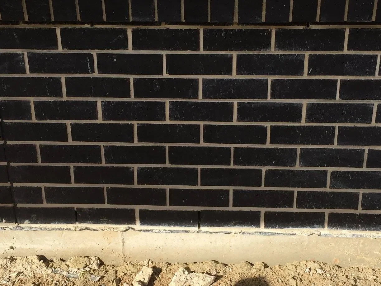 Black brick wall at ground level with dirt and concrete in the foreground.
