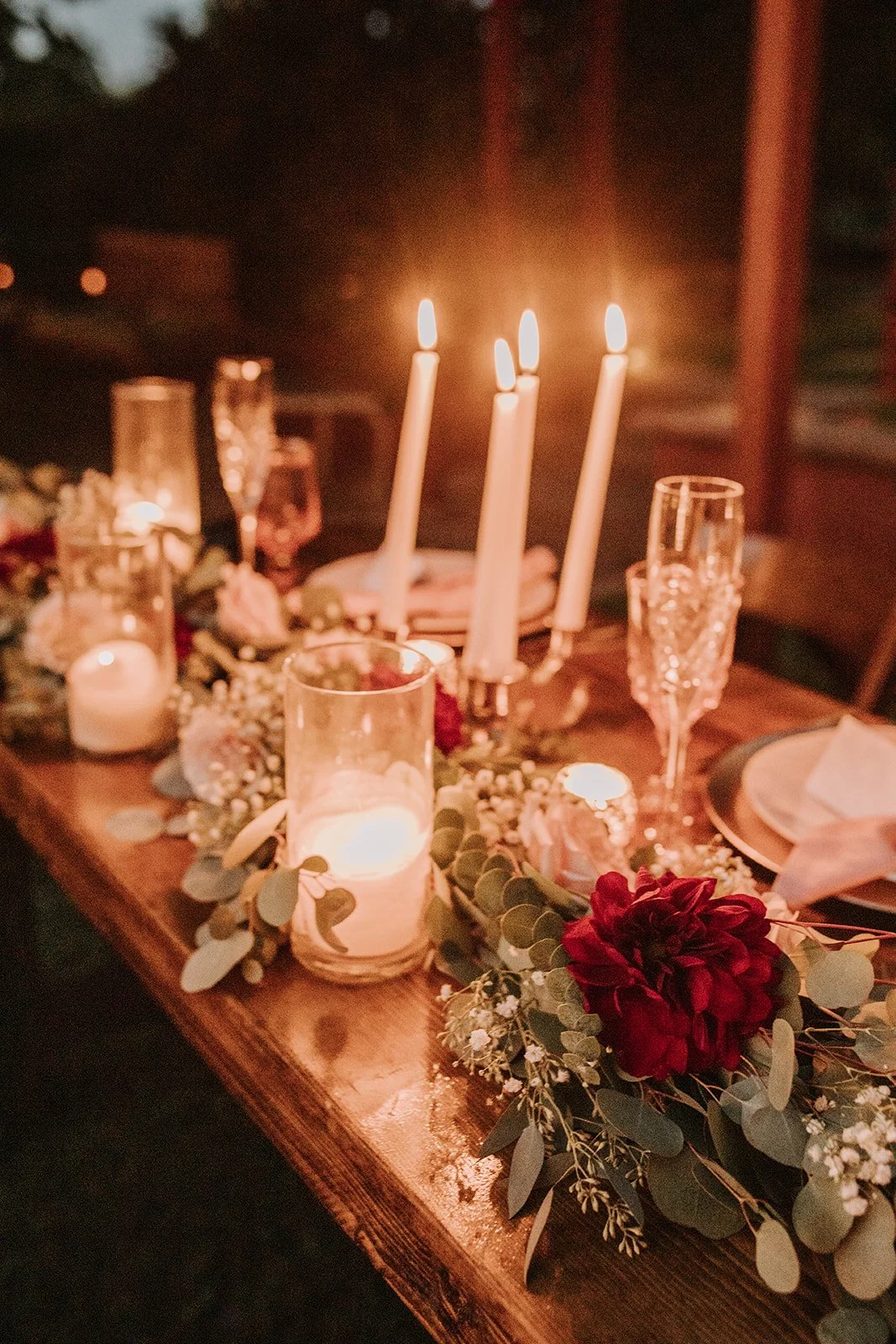 A beautifully decorated table with lit candles, floral arrangements, and glassware for a romantic or elegant dinner setting.