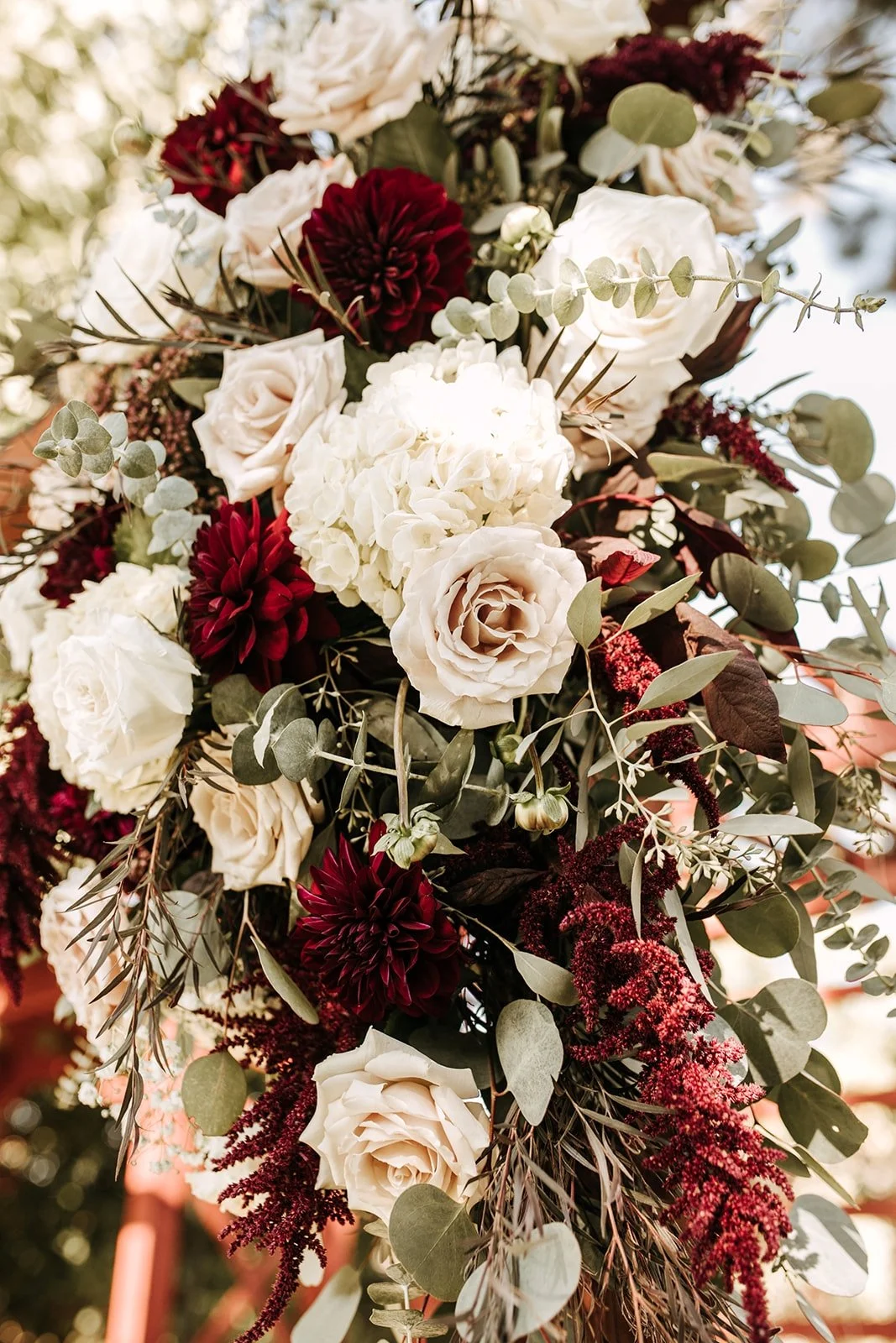 Close-up of a floral arrangement with white roses, deep red dahlias, white hydrangeas, and greenery.