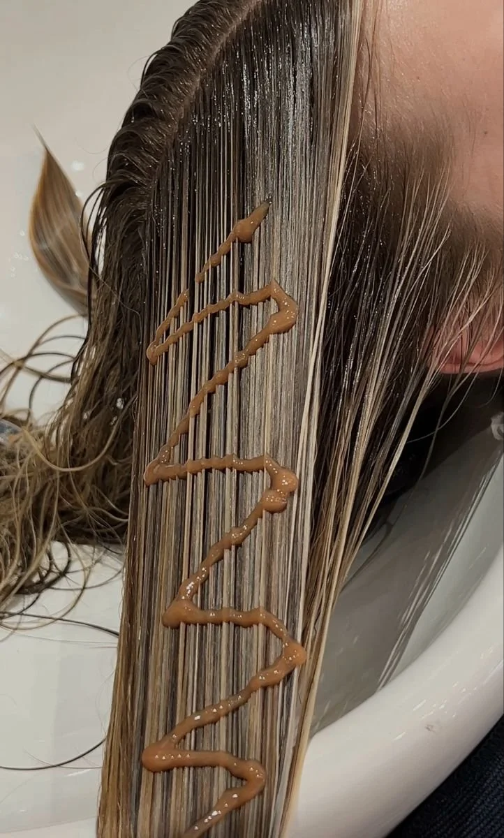 A person's hair being washed in a salon sink with the word 'RELAX' written on it with brown hair dye or conditioner.
