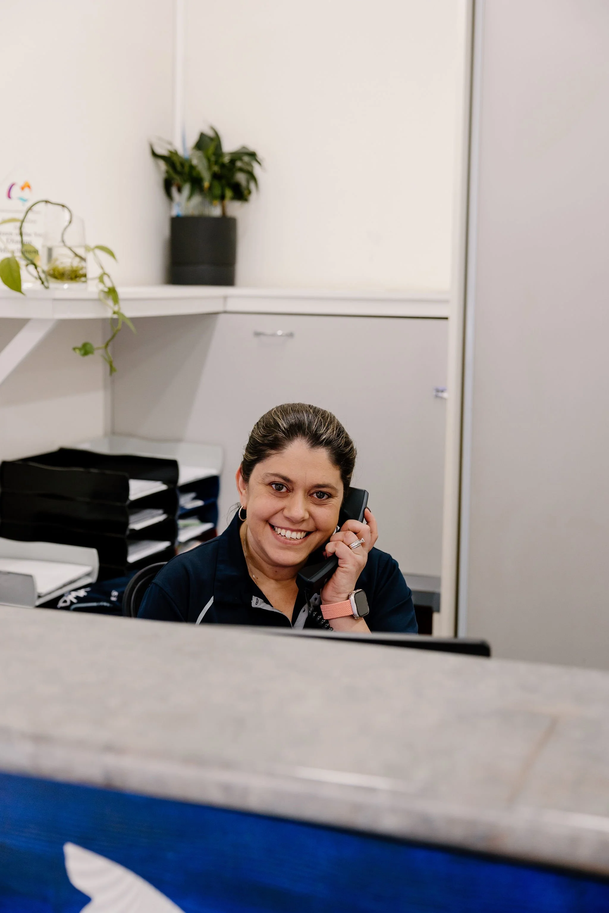 A woman smiling while talking on the phone at a workplace desk.