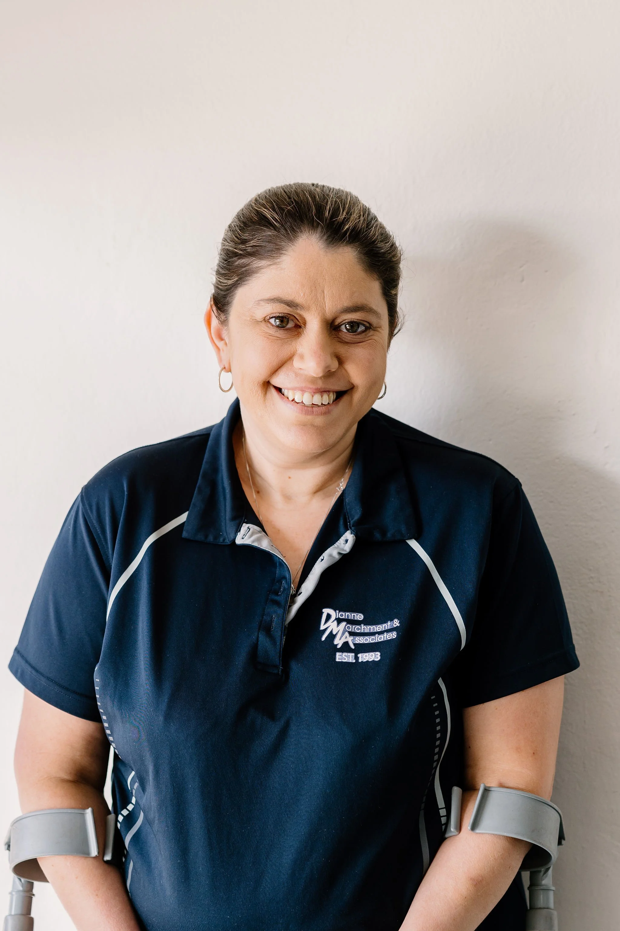 Tamara smiling in a navy blue polo shirt with a company logo, standing against a plain wall.