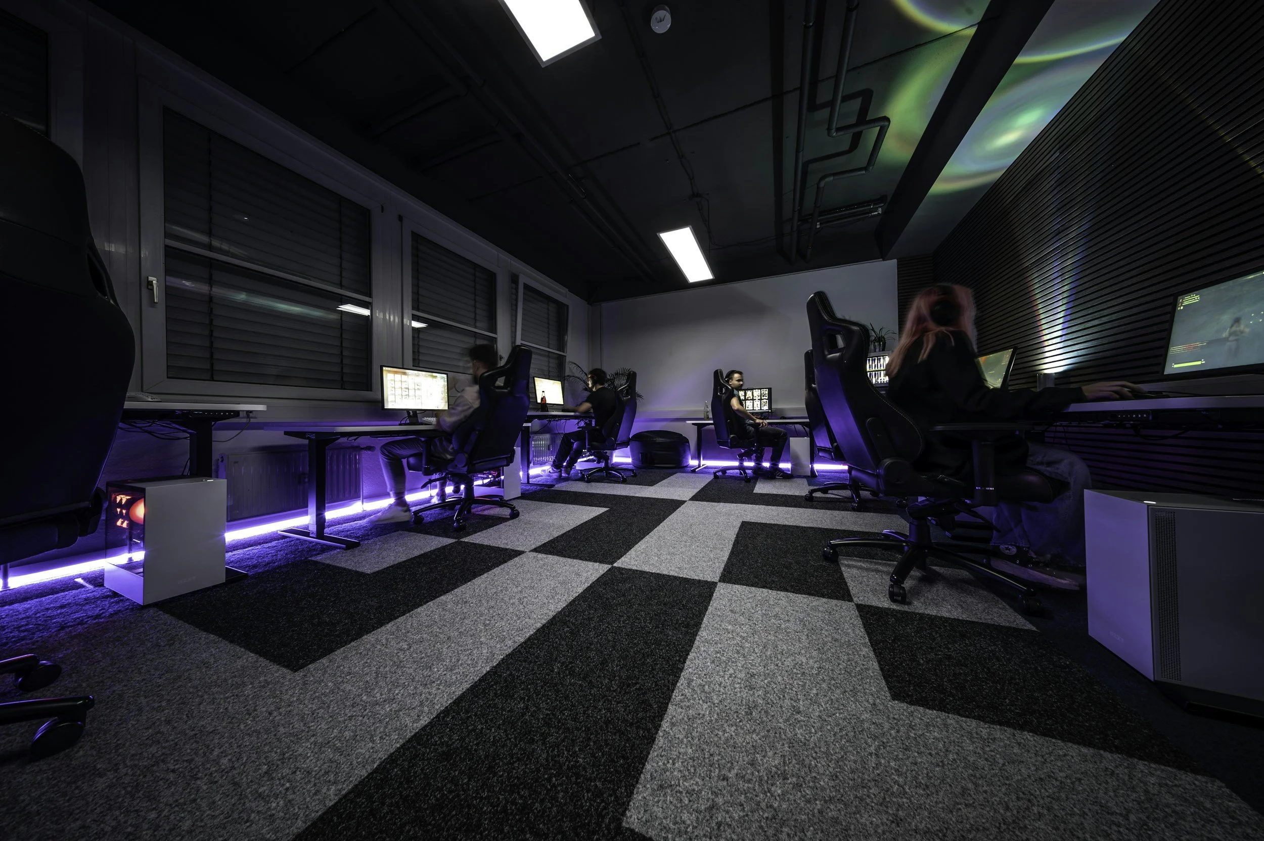 A group of people playing video games at a modern esports gaming center, with gaming chairs, monitors, and blue LED lighting.
