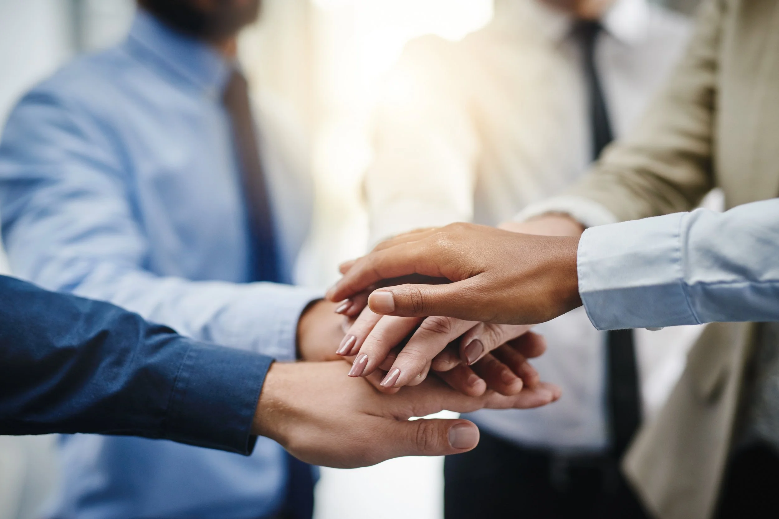 Multiple people with different skin tones stacking hands together in a gesture of teamwork and unity.